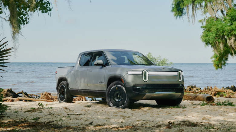 Silver Rivian R1T pickup truck seen from right front on beach