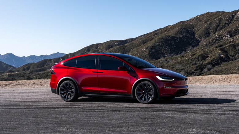 Red Tesla Model X SUV seen from the right on a desert road with mountain background