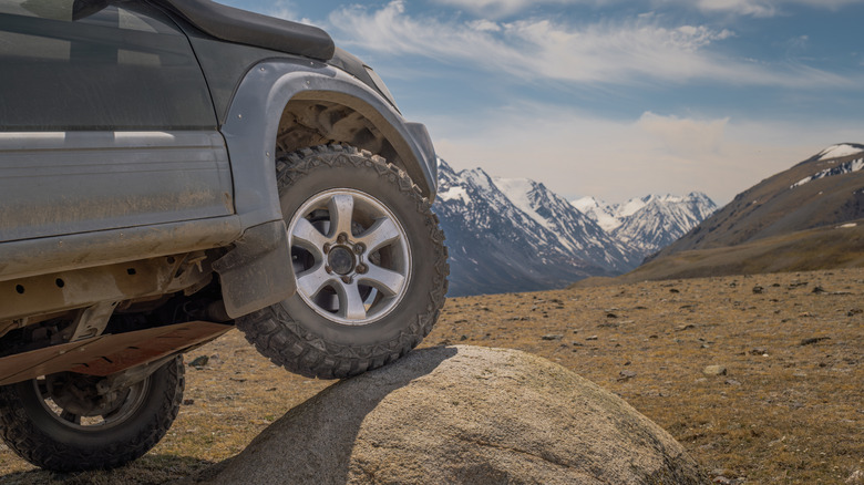 A car with one wheel on top of a rock, causing it to tilt