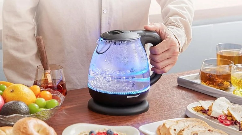 man holding Elite Gourmet Electric Kettle among a big breakfast