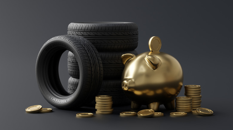 A golden piggy bank and coins sitting next to a stack of three tires and another tire standing on its side.