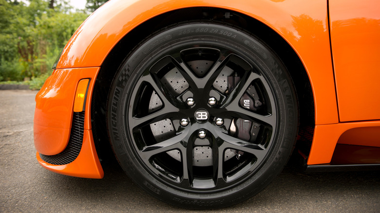 A close-up of a bright orange Bugatti Veyron's Michelin Pilot Sport Pax tires on shiny black rims.