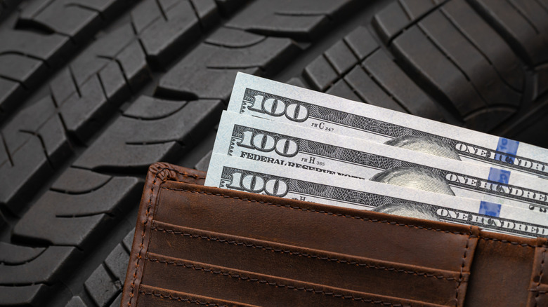 Three one-hundred dollar bills poking out of a wallet, against a background made of tire tread