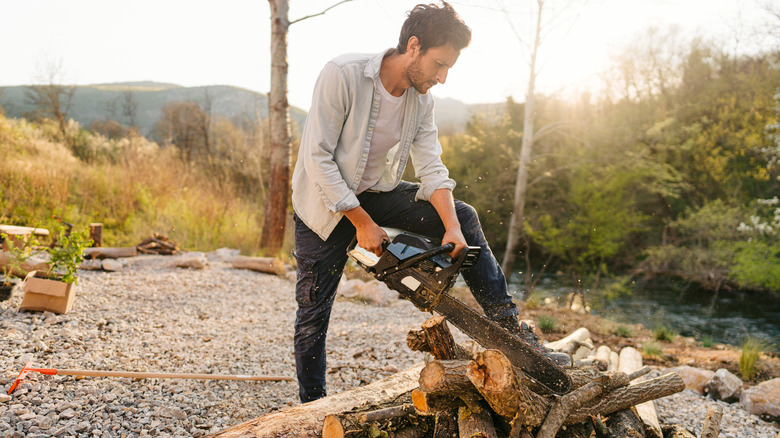 Man uses chainsaw on log pile
