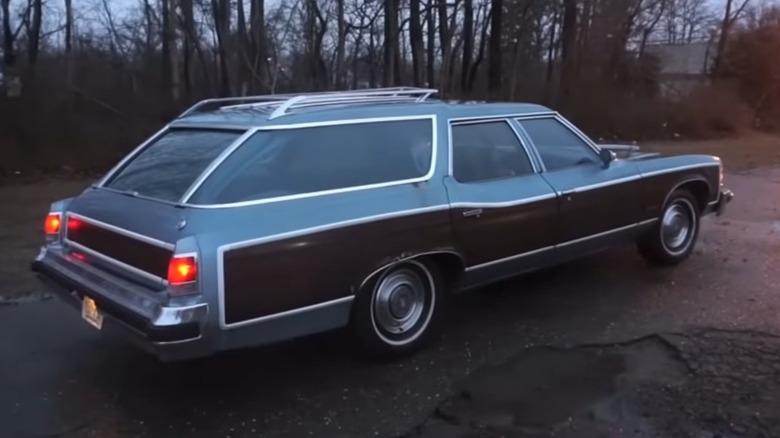 A blue and brown Pontiac Grand Safari station wagon parked in a private driveway, in the evening with trees in the back.