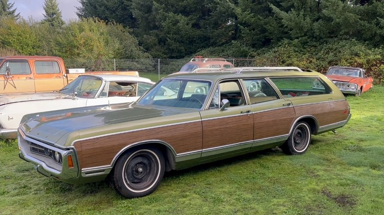 A pea-green Dodge Royal Monaco Station wagon with brougham wood paneling parked on grass with other classic cars.