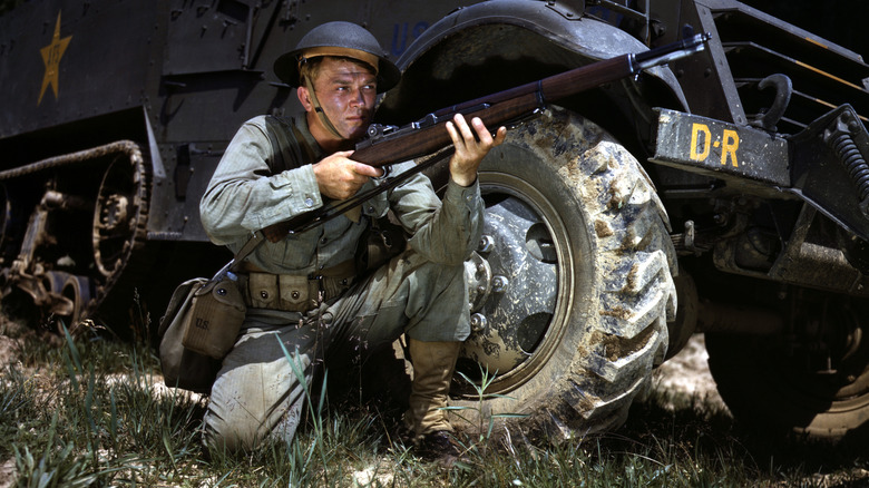 World War II Infantryman, kneeling in front of M3 Half-track, holds an M1 Garand rifle at the ready. Fort Knox, Kentucky, June 1942.