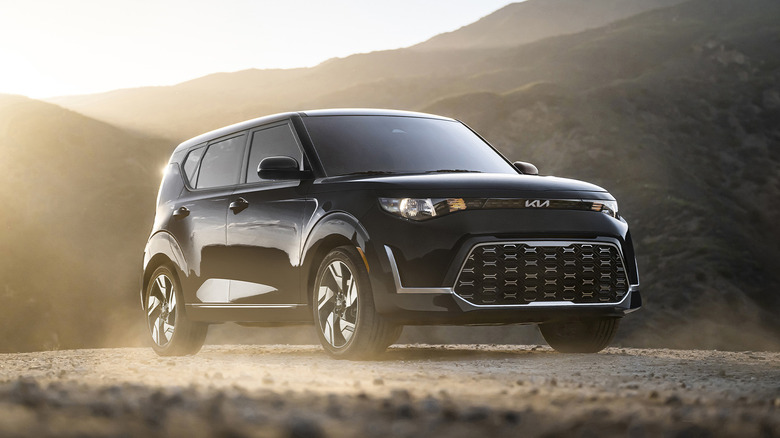 A black Kia Soul parked by some hills