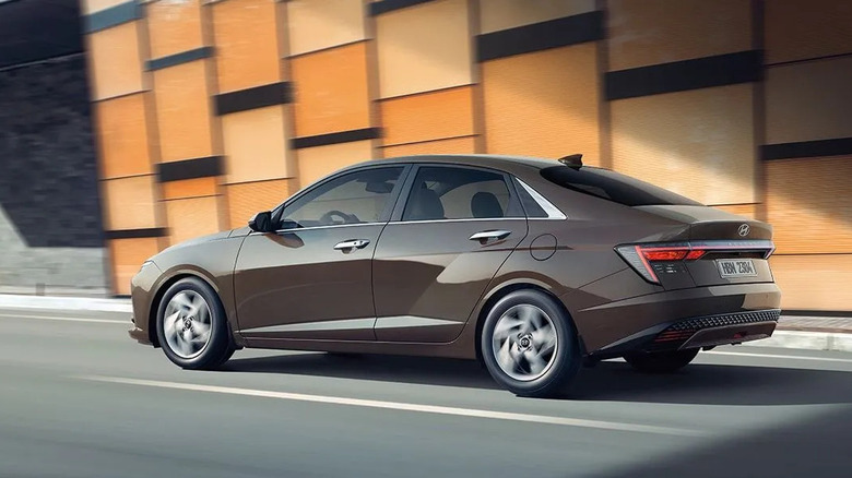 Hyundai Accent compact sedan driving along a modern city street with a backdrop of geometric orange
