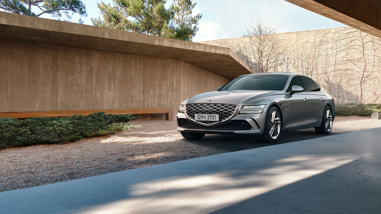 Genesis G80 luxury sedan parked in a modern architectural setting with natural landscaping and minimalist concrete structures.
