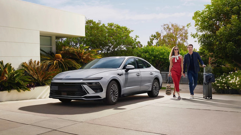 2025 Hyundai Sonata Hybrid parked in a modern driveway as a stylish couple with luggage walks past