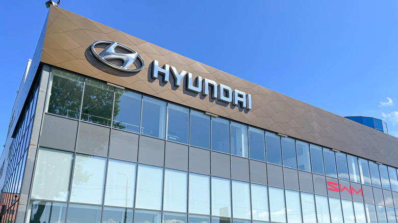 Modern glass-fronted car dealership building displaying Hyundai and SWM logos under a clear blue sky.