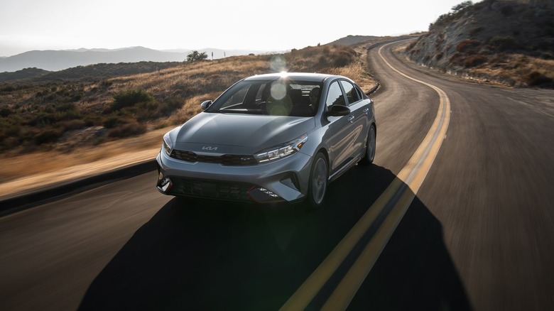 A grey 2024 Kia Forte zooming down a mountain road, brown hills visible in the background