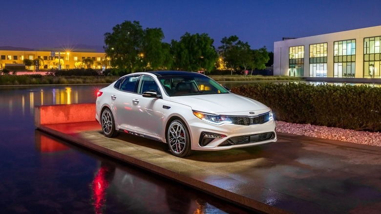 A white Kia Optima for the 2020 Model year on a platform next to a water feature