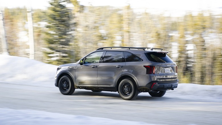 A slate grey mushroom Kia Sorento 2025 zooming along a forested snowy road in the morning