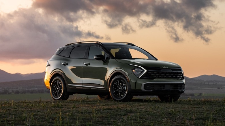 A military green Kia Sportage 2025 in a field against a dusk skyline.