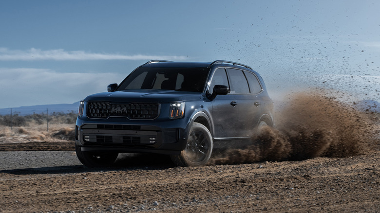 A navy blue 2025 Kia Telluride that's on gravel and throwing up dirt behind it