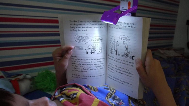 Child in bed reading a book with a light shining on the pages