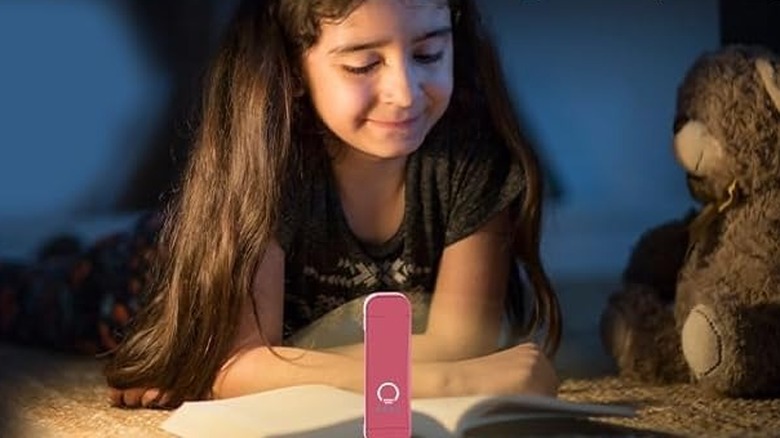 Young girl reading a book lit up by a pink light