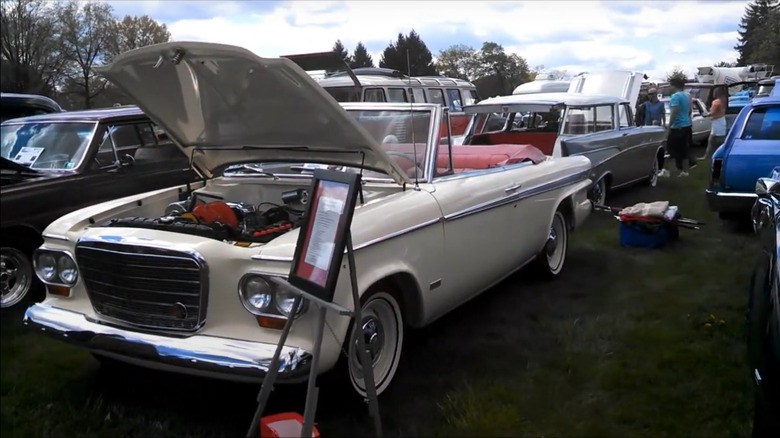 A cream colored 1962 Studebaker Super Lark Convertible parked at an auto show with its bonnet open