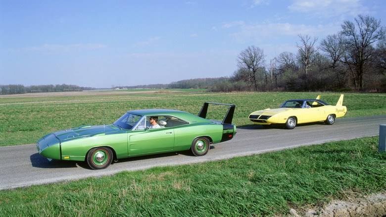 A rust orange Plymouth Superbird alongisde a lovely Dodge Charger Daytona, both seen on a backcountry road