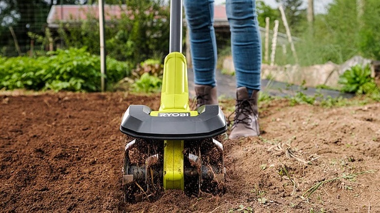 Using a Ryobi cultivator to break down soil on land.