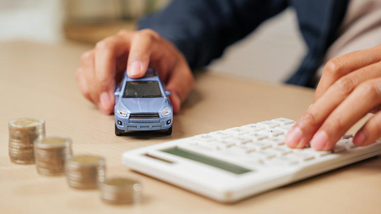 calculator and toy car in front of coin stacks