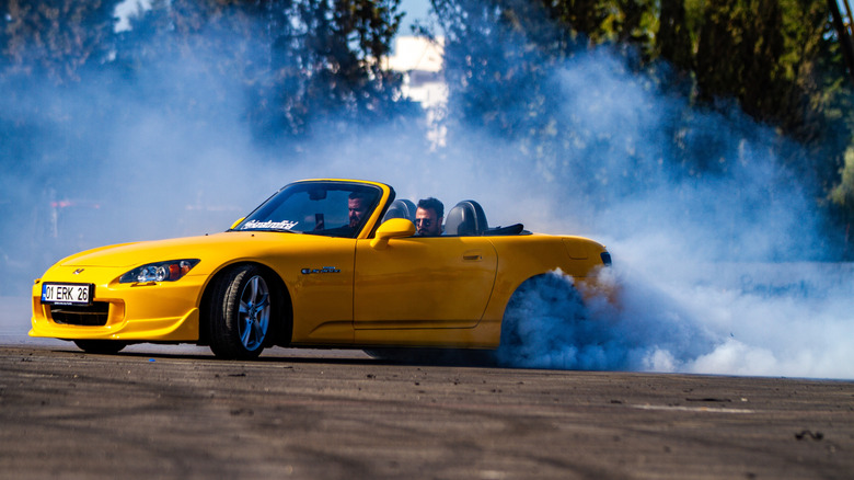 Yellow Honda S2000 doing a burnout in a parking lot