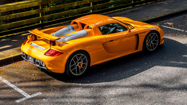 Orange Porsche Carrera GT parked in parking spot by wooden fence