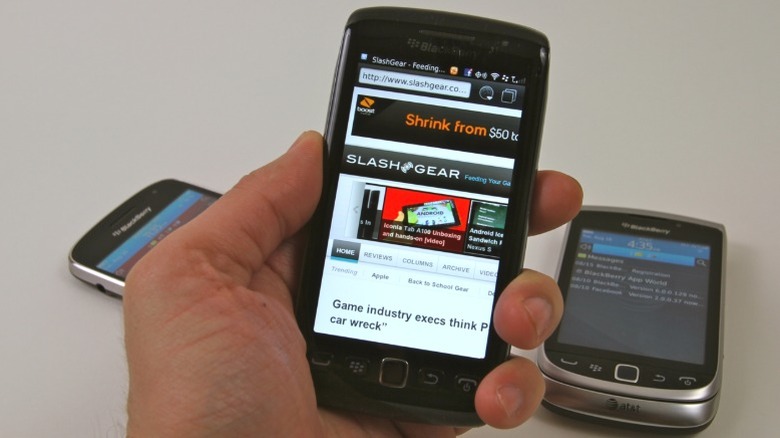 Hand holding BlackBerry Torch 9850 with two other BlackBerry phones in the background