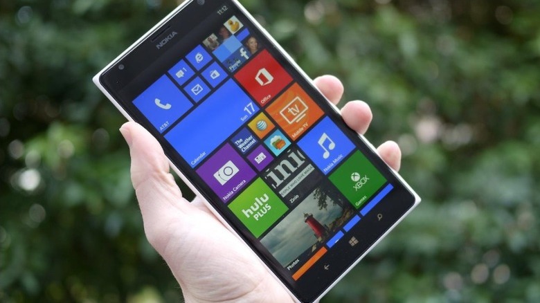 Hand holding up a Nokia Lumia 1520 with greenery in the background