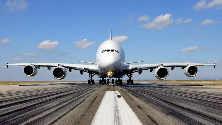 Front view of Airbus A380 jumbo jet preparing for takeoff on runway, showcasing its four-engine layout and massive double-deck fuselage under a clear blue sky.