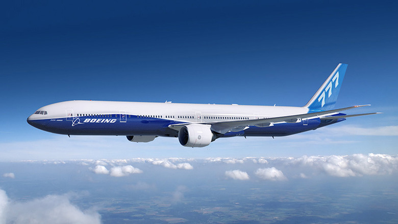 Boeing 777 wide-body jet cruising at high altitude, showcasing sleek aerodynamic design and Boeing livery above a layer of clouds.