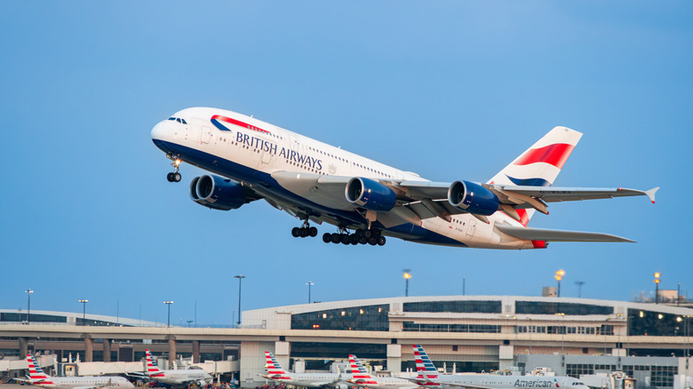 A British Airways liveried A380 taking off, airport visible in the background