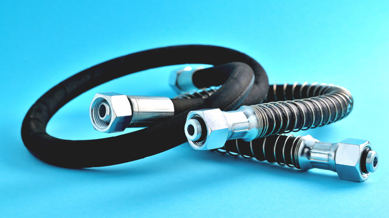 Close-up of flexible automotive brake hoses with metal fittings on a sky blue background.