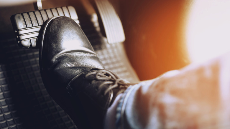 Close-up of a driver wearing a brown dress shoe pressing down on a car's brake pedal.