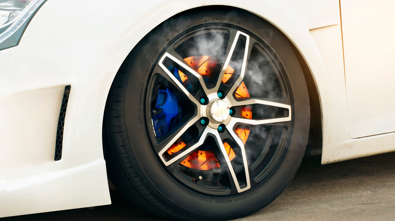 Close-up of a car wheel with glowing hot brake rotors and smoke, showing signs of overheated or locked-up brakes.