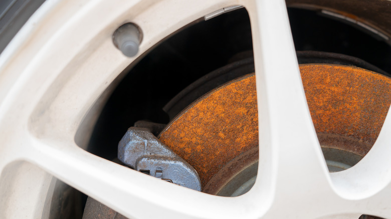 Close-up of a car's rusty brake rotor and caliper visible through the wheel.