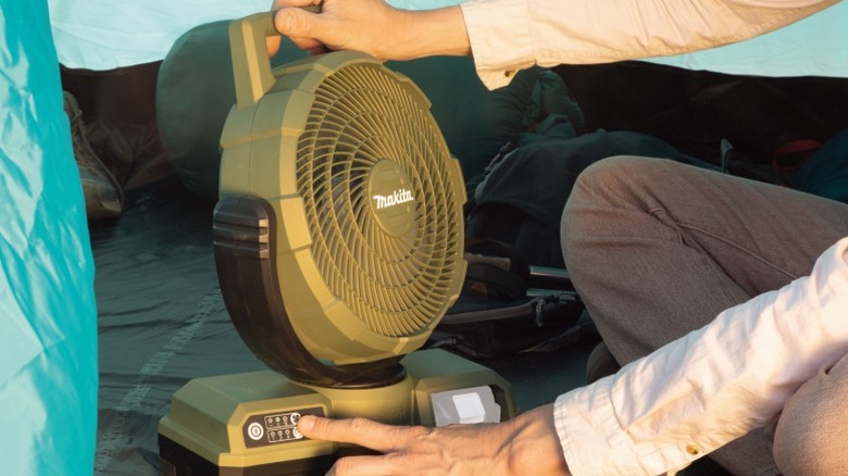 Person adjusting a Makita Outdoor Adventure 18V LXT Cordless/Corded 9-¼-inch Fan inside a tent