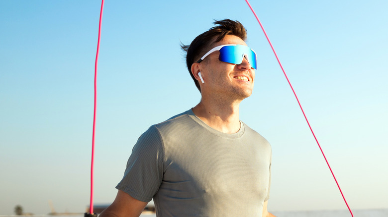 A smiling man with earbuds, skipping on a rope