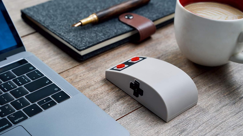 The 8Bitdo N30 Wireless Mouse next to a laptop and a cup of coffee on a wooden desktop