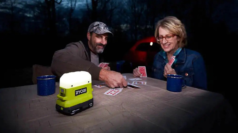 People playing cards near a Ryobi Compact Area Light