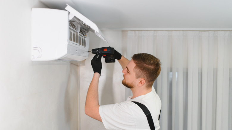A repair technician unscrewing the air filters on an AC unit