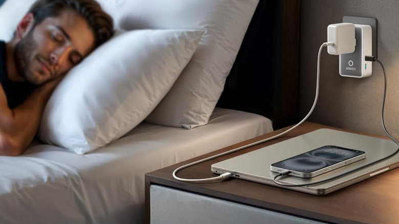 A man sleeping in a hotel while his Anker Nano charges his devices.
