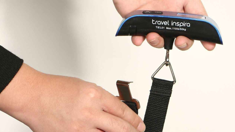 A person tying a Travel Inspira luggage scale on a bag.