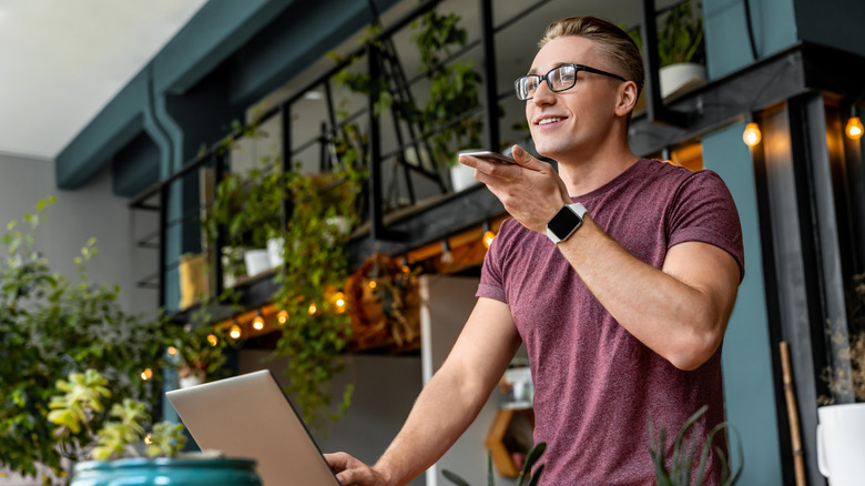 Man talking into smartphone standing in front of a laptop