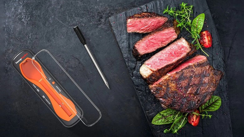 Sliced roast with grill marks on a black cutting board next to a meat thermometer