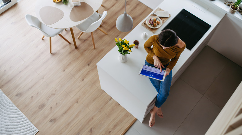 Woman sitting on kitchen counter programming a smart home device on a tablet