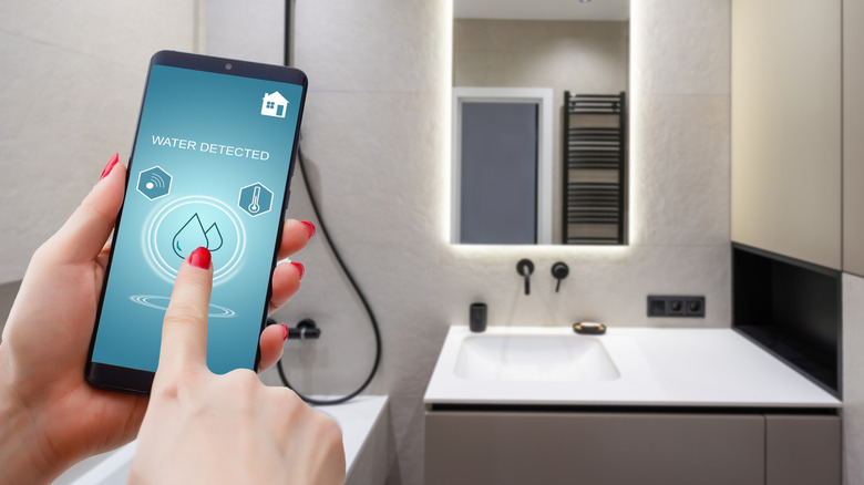 Hand tapping a smartphone screen displaying "water detected"