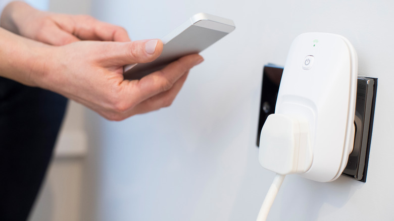 Person holding a smartphone close to a white smart plug